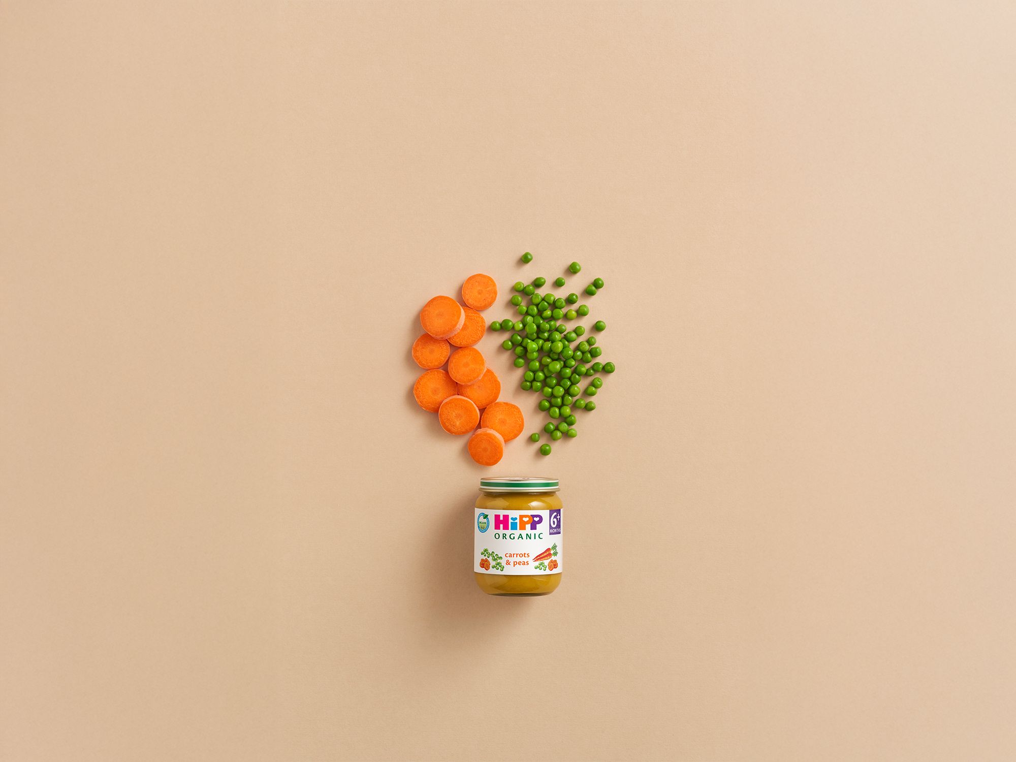 HiPP Organic Carrots & Peas baby food jar with sliced carrots and peas arranged above on a neutral background