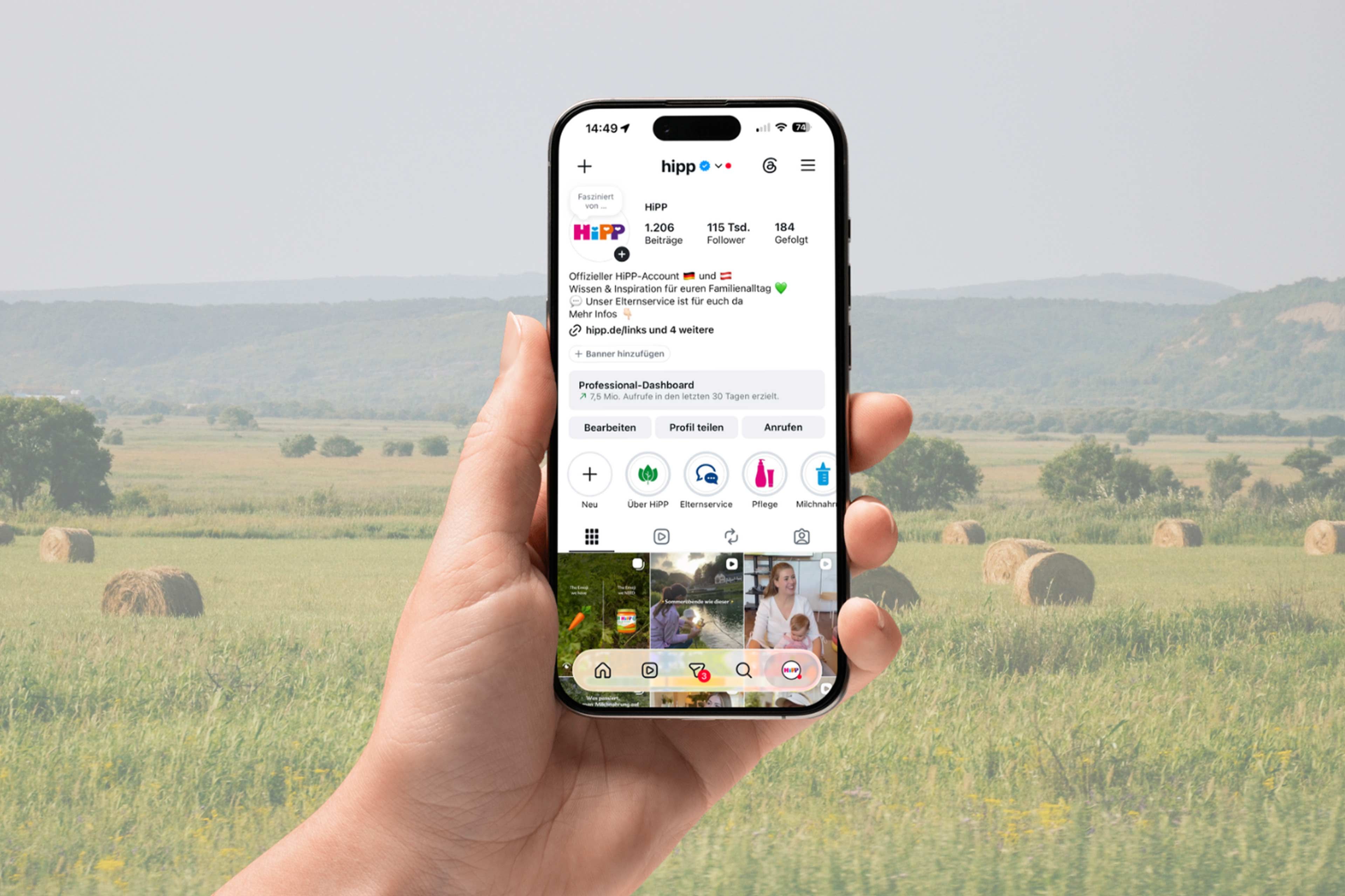 Hand mit Smartphone, auf dem der HiPP Social-Media-Account vor einer grünen, ländlichen Wiesenlandschaft geöffnet ist