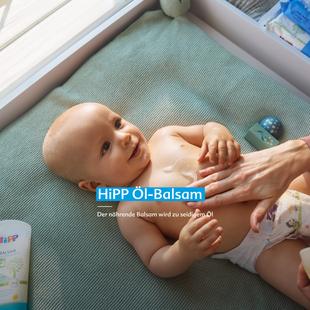 Lächelndes Baby auf Wickelauflage, dessen Bauch mit HiPP HOCHVERTRÄGLICH Öl-Balsam sanft eingecremt wird