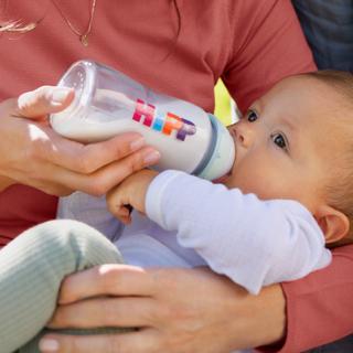 Baby wird von einer Person im roten Pullover mit einer Flasche HiPP-Milch gefüttert