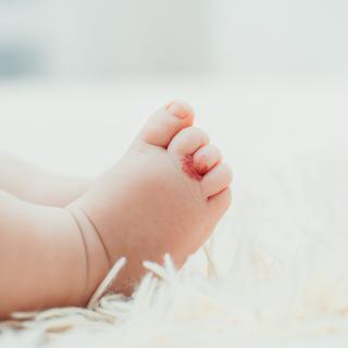 Babyfuß mit einem roten Fleck auf einer weißen, flauschigen Oberfläche.