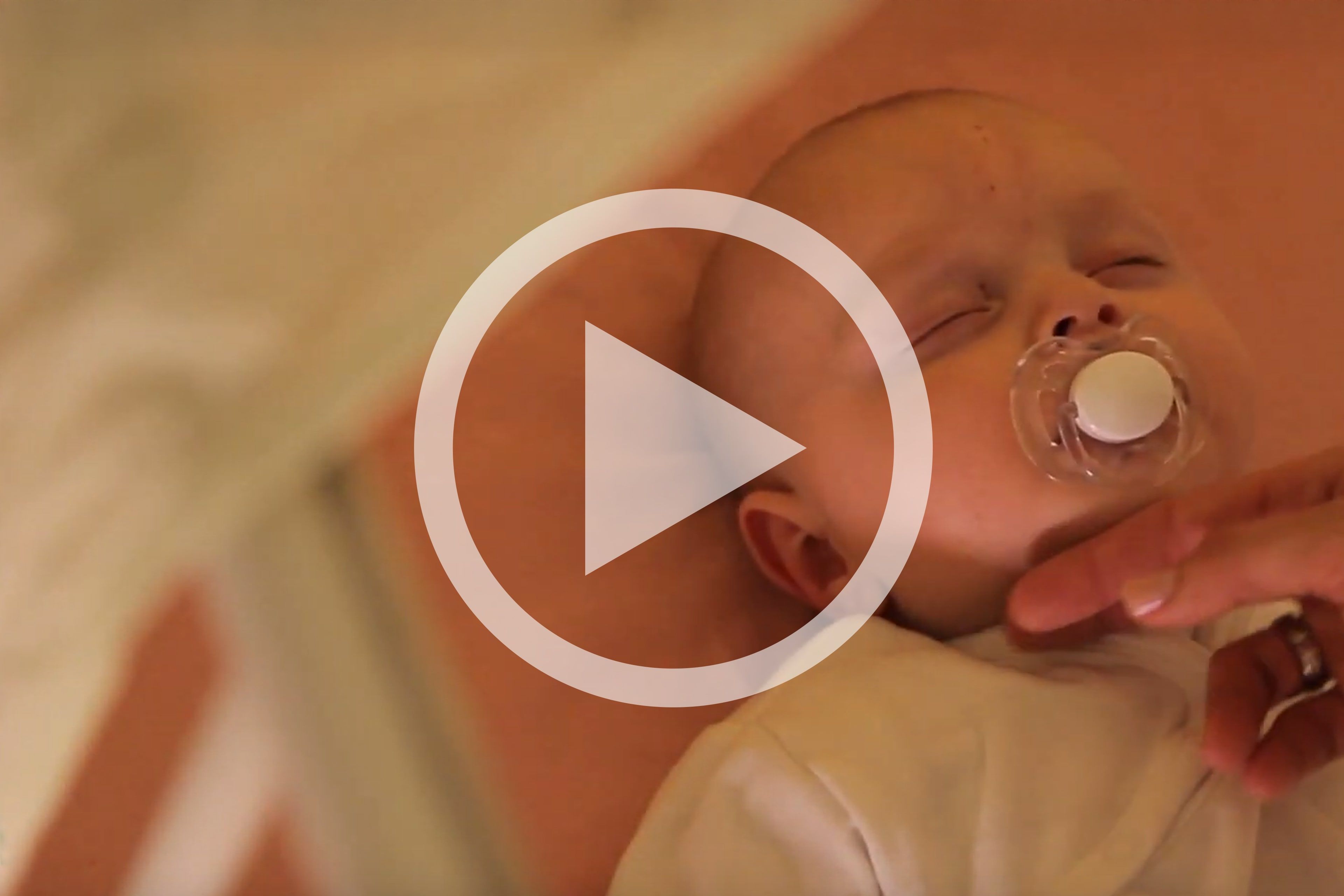 Baby liegt in weißem Strampler auf einer Decke und wird von einer Hand berührt