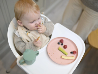 Baby eating toast and fruit in a highchair