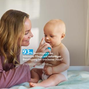 Frau mit langem Haar sitzt neben einem nackten Baby auf einer Decke und berührt lächelnd dessen Nase