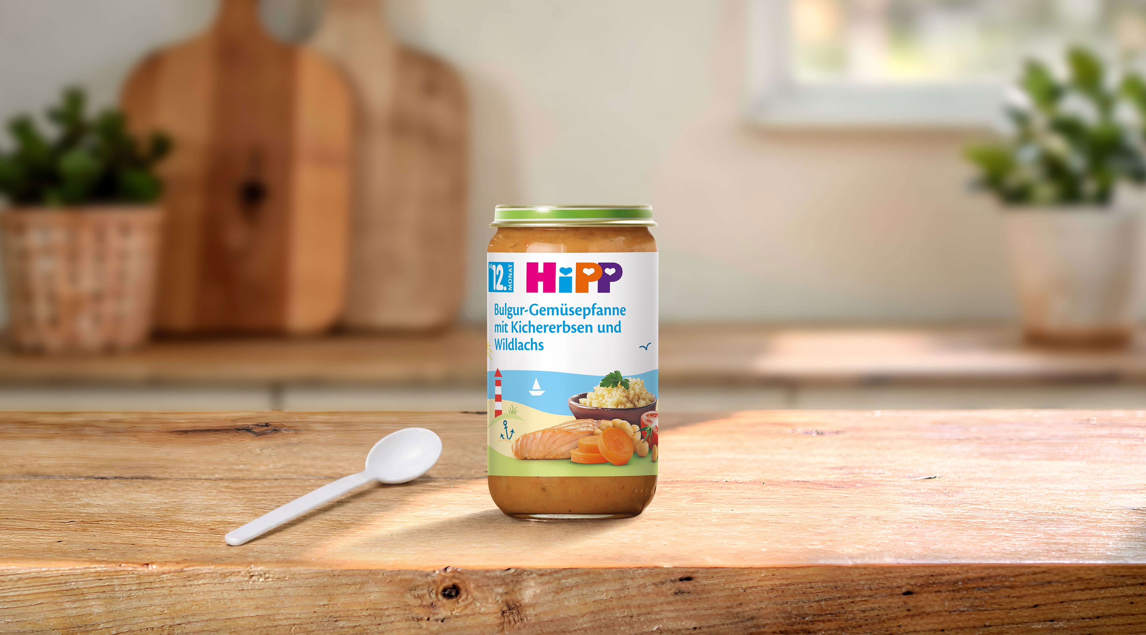 HiPP Gläschen Bulgur-Gemüsepfanne mit Kichererbsen und Wildlachs ab dem 12. Monat neben einem Löffel