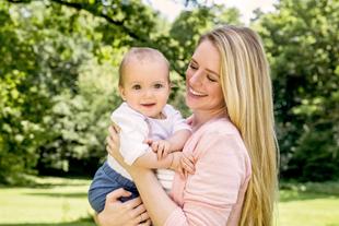 Ein freudiger Moment zwischen einer Mutter und ihrem Baby vor einer üppigen grünen Kulisse.