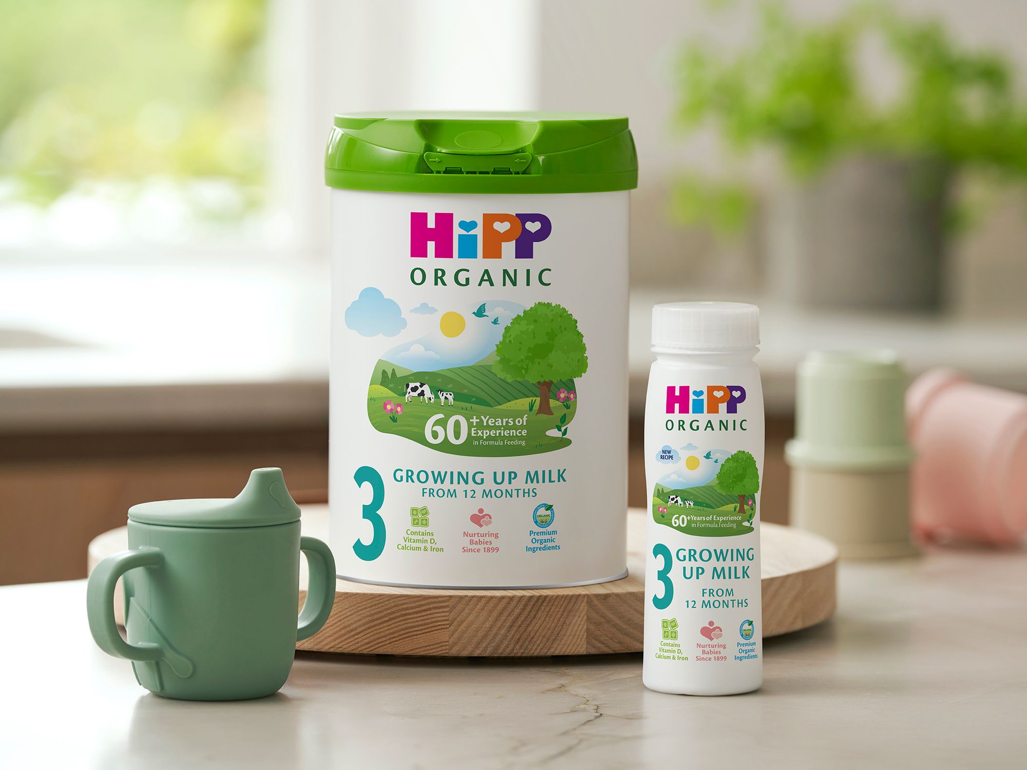 HiPP Organic growing up milk tub and ready-to-feed bottle on a kitchen counter beside a green toddler beaker
