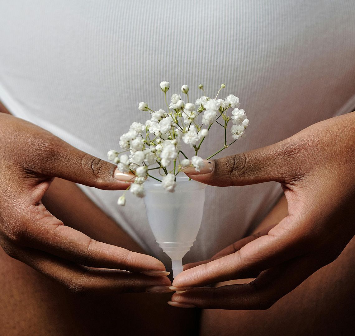 Hands gently holding a menstrual cup filled with delicate white flowers in front of the lower abdomen.