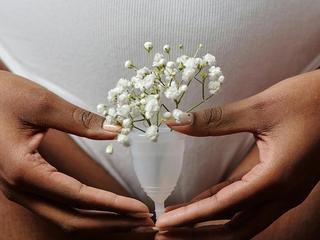 Hands gently holding a menstrual cup filled with delicate white flowers in front of the lower abdomen.