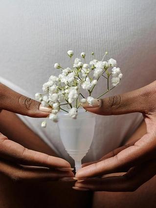 Hands gently holding a menstrual cup filled with delicate white flowers in front of the lower abdomen.