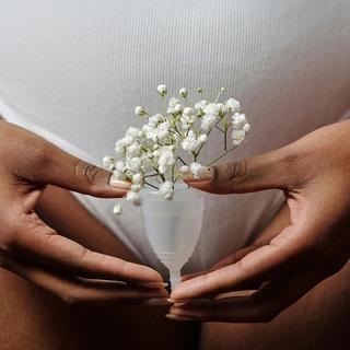 Hands gently holding a menstrual cup filled with delicate white flowers in front of the lower abdomen.