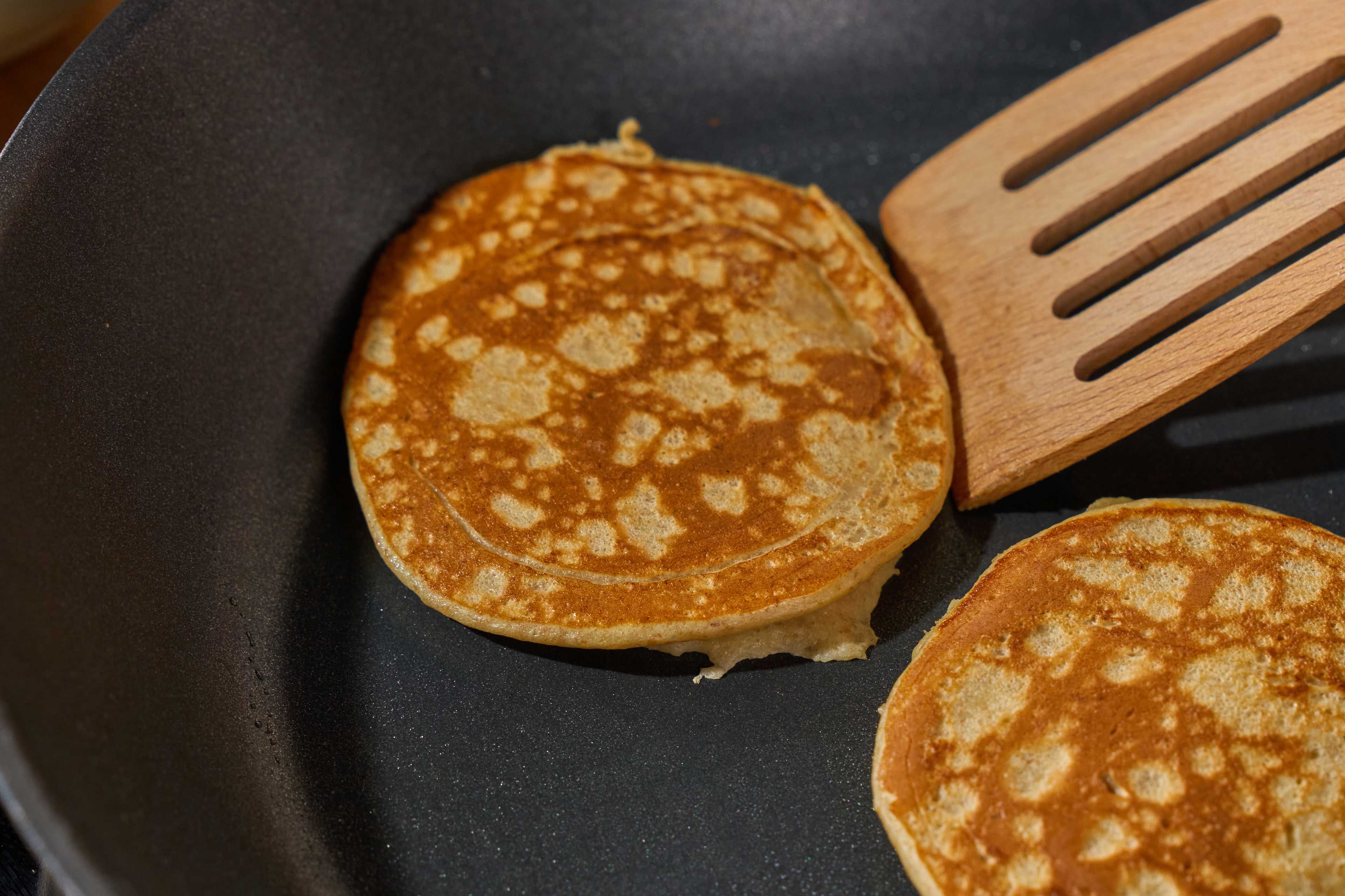 Zwei goldbraune Pfannkuchen in einer Pfanne mit einem Holzwender