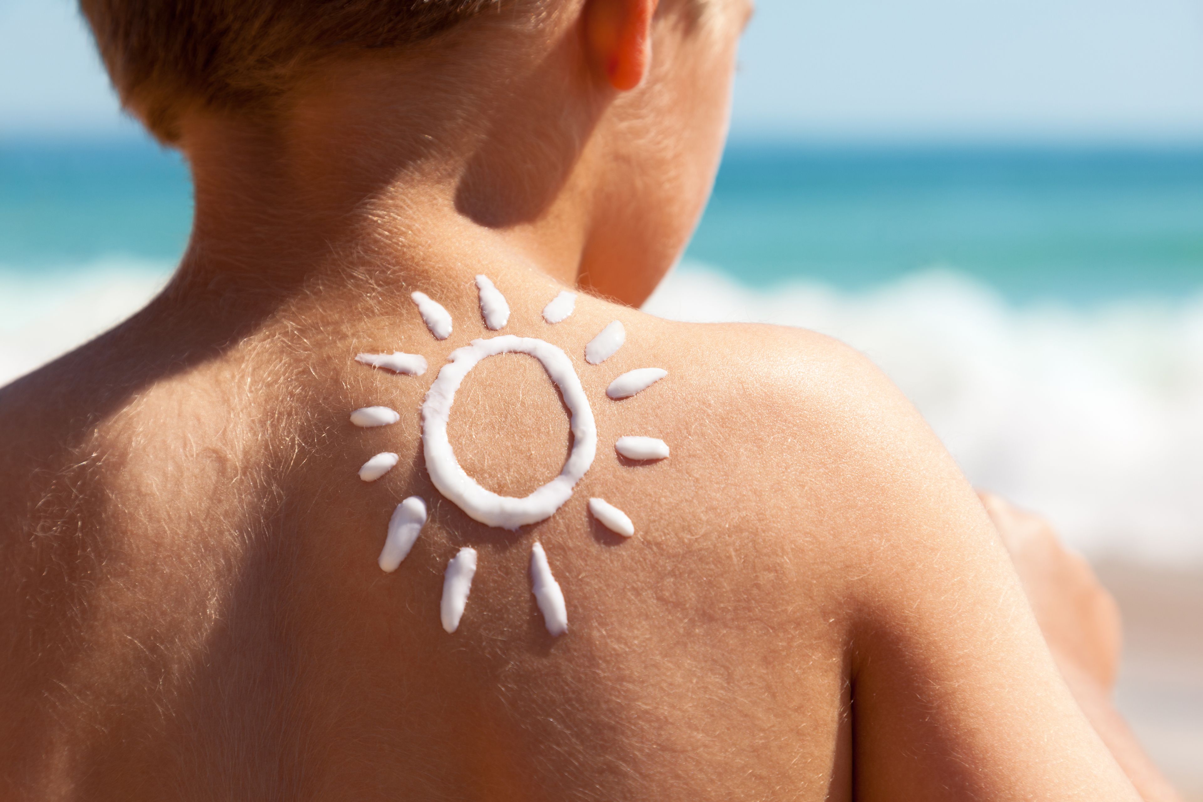 Der Rücken einer Person mit Sonnenschutzmittel in Form einer Sonne, mit dem Meer im Hintergrund.