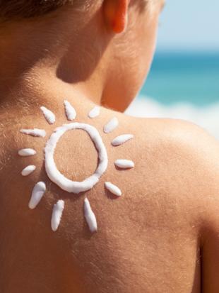 Der Rücken einer Person mit Sonnenschutzmittel in Form einer Sonne, mit dem Meer im Hintergrund.
