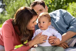 Eltern kuscheln im Grünen mit ihrem Baby und schenken ihm Nähe für eine gesunde Darmflora und Entwicklung.