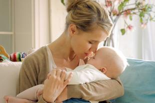 Ein zärtlicher Moment zwischen einer Mutter und ihrem Baby, in dem die Mutter sanft die Stirn des Babys küsst.