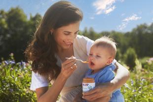 Mutter füttert ihr Baby im Grünen mit HiPP Bio-Gemüsebrei aus dem Gläschen – Vertrauen in 70 Jahre Bio-Spitzenqualität.