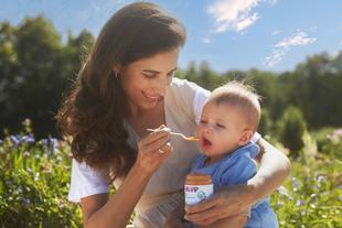 Mutter füttert ihr Baby im Grünen mit HiPP Bio-Gemüsebrei aus dem Gläschen – Vertrauen in 70 Jahre Bio-Spitzenqualität.
