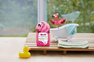 Flasche mit Flamingo-Motiv und der Aufschrift 'HiPP Blubber Bad' steht neben einer kleinen Badewanne mit Handtuch, einer gelben Quietscheente und einer gezeichneten Flamingofigur.