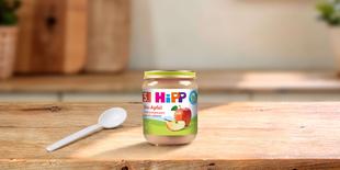HiPP Bio-Apfel Babygläschen mit Apfelpüree und Löffel auf einem Holztisch in heller Küchenumgebung