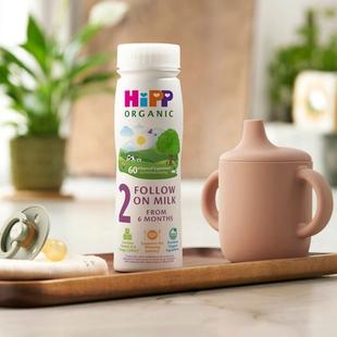 HiPP Organic follow on milk ready to feed bottle on a tray beside a pastel sippy cup and dummy on a bright kitchen worktop