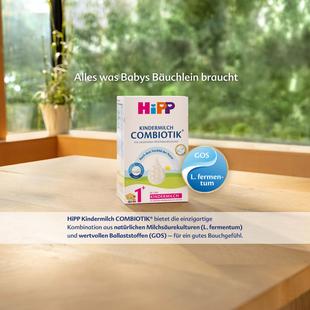 Packung HiPP Kindermilch COMBIOTIK auf Holztisch vor grünem Fensterhintergrund mit Text und blauen Kreisen 'GOS' und 'L. fermentum'
