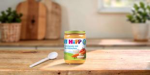 HiPP Bio-Gläschen „Gemüsereis mit Bio-Hühnchen“ ab dem 5. Monat auf Holztisch mit Löffel in heller Küchenumgebung