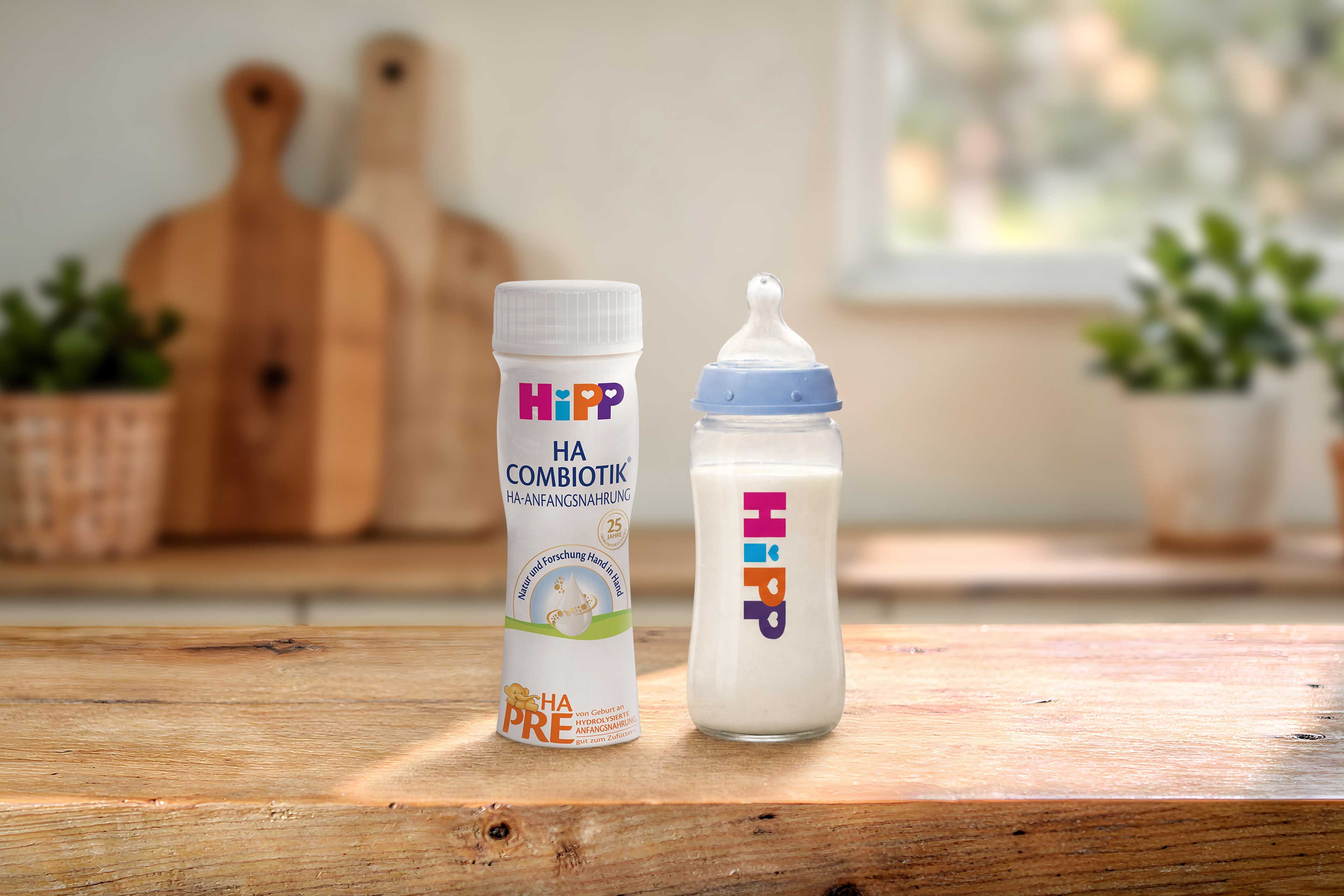 HiPP PRE HA COMBIOTIK® trinkfertige 200ml Flasche neben gefülltem Babyfläschchen auf Holztisch in heller Küche