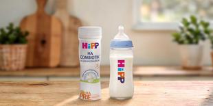 HiPP PRE HA COMBIOTIK® trinkfertige 200ml Flasche neben gefülltem Babyfläschchen auf Holztisch in heller Küche