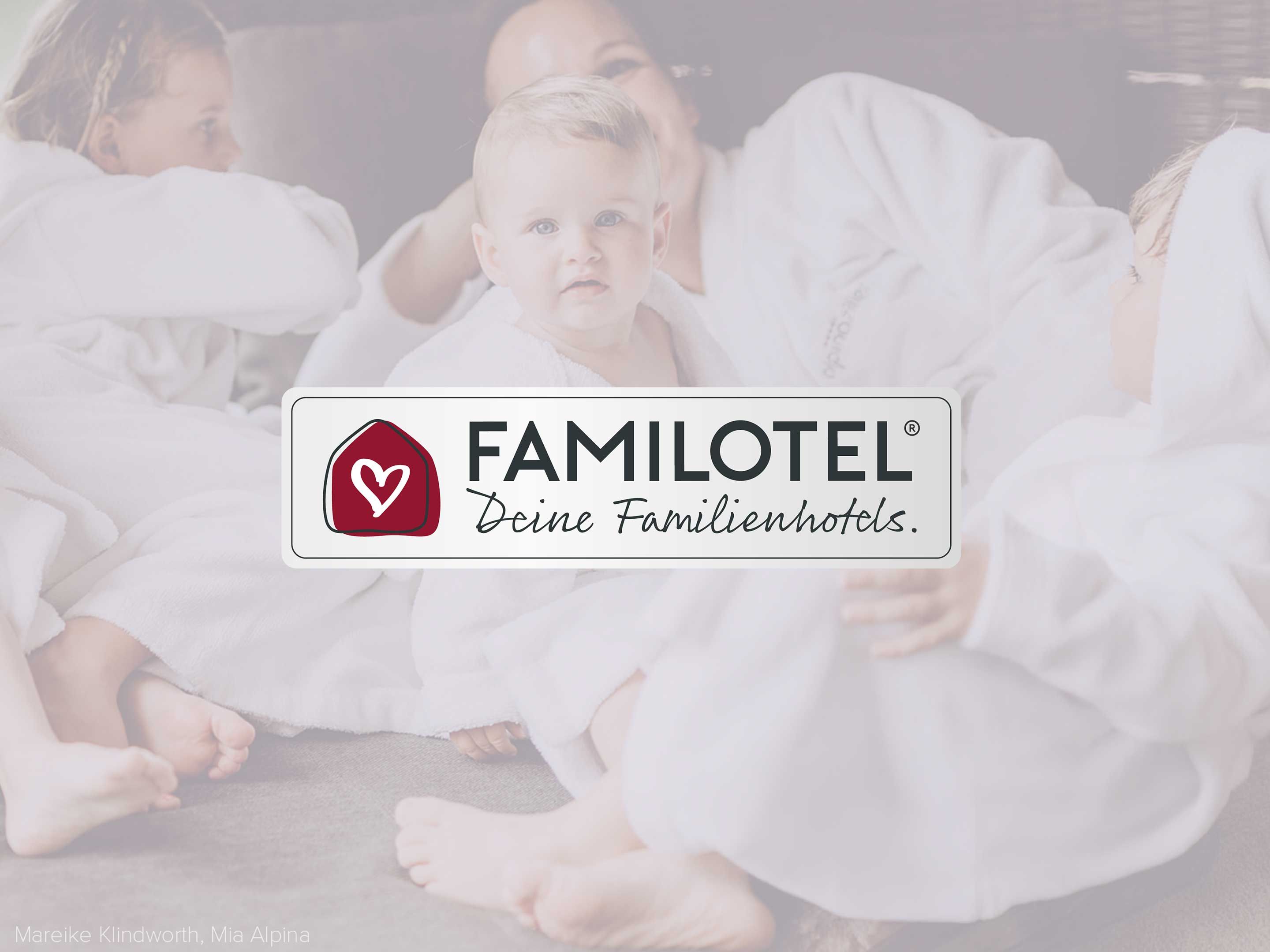 Familie kuschelt mit Baby im Bett, im Vordergrund das Familotel-Logo