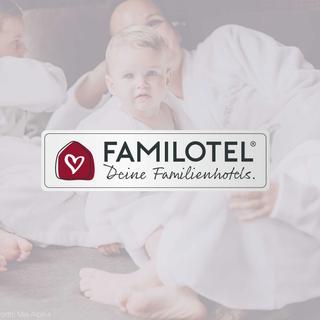 Familie kuschelt mit Baby im Bett, im Vordergrund das Familotel-Logo