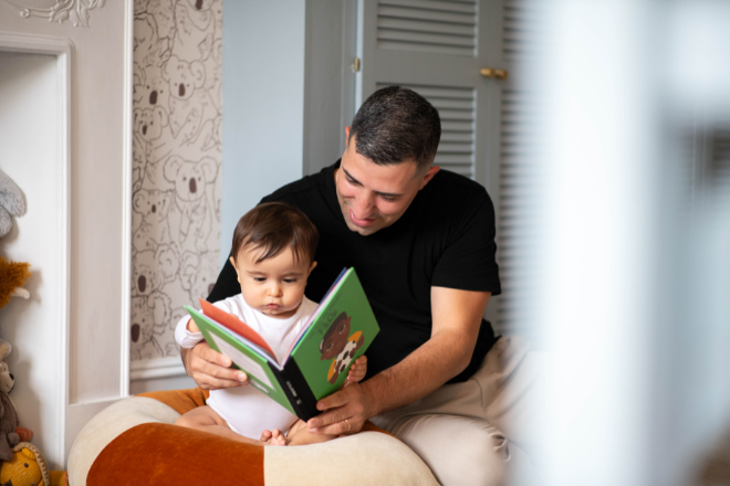 Dad reading book to 10-month old baby in bedroom