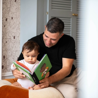 Dad reading book to 10-month old baby in bedroom