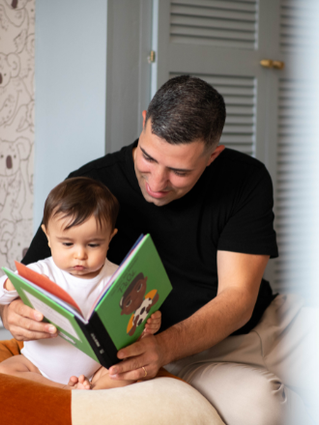 Dad reading book to 10-month old baby in bedroom