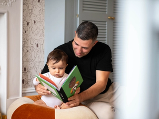 Dad reading book to 10-month old baby in bedroom