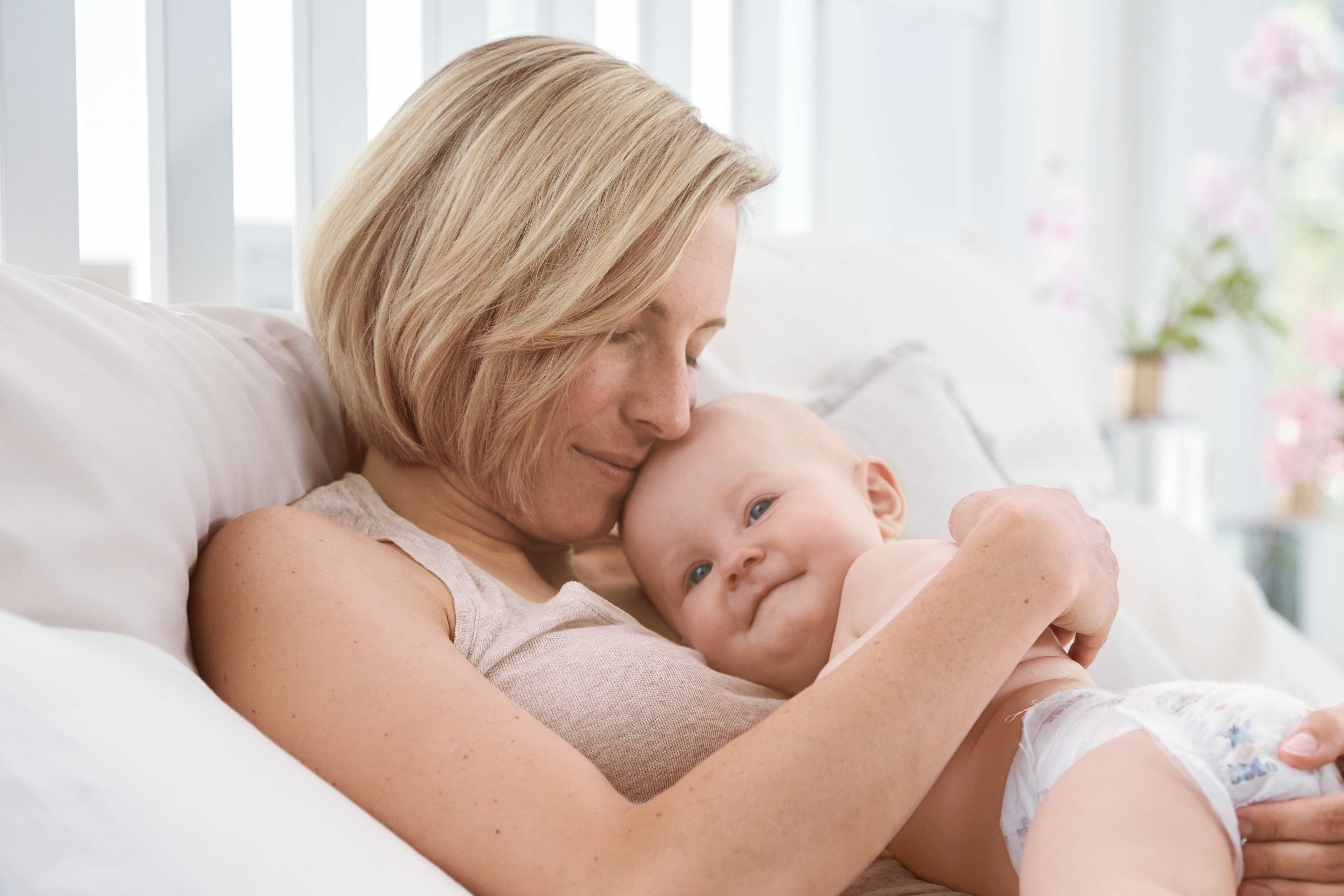 Ein zärtlicher Moment zwischen einer Mutter und ihrem Baby, wobei die Mutter das Baby sanft an ihr Gesicht drückt.