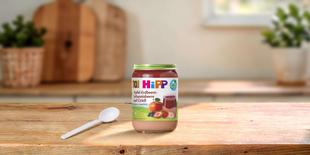 HiPP Bio-Gläschen Apfel-Erdbeere-Johannisbeere auf Grieß ab 10 Monaten auf Holztisch mit Löffel in heller Küche