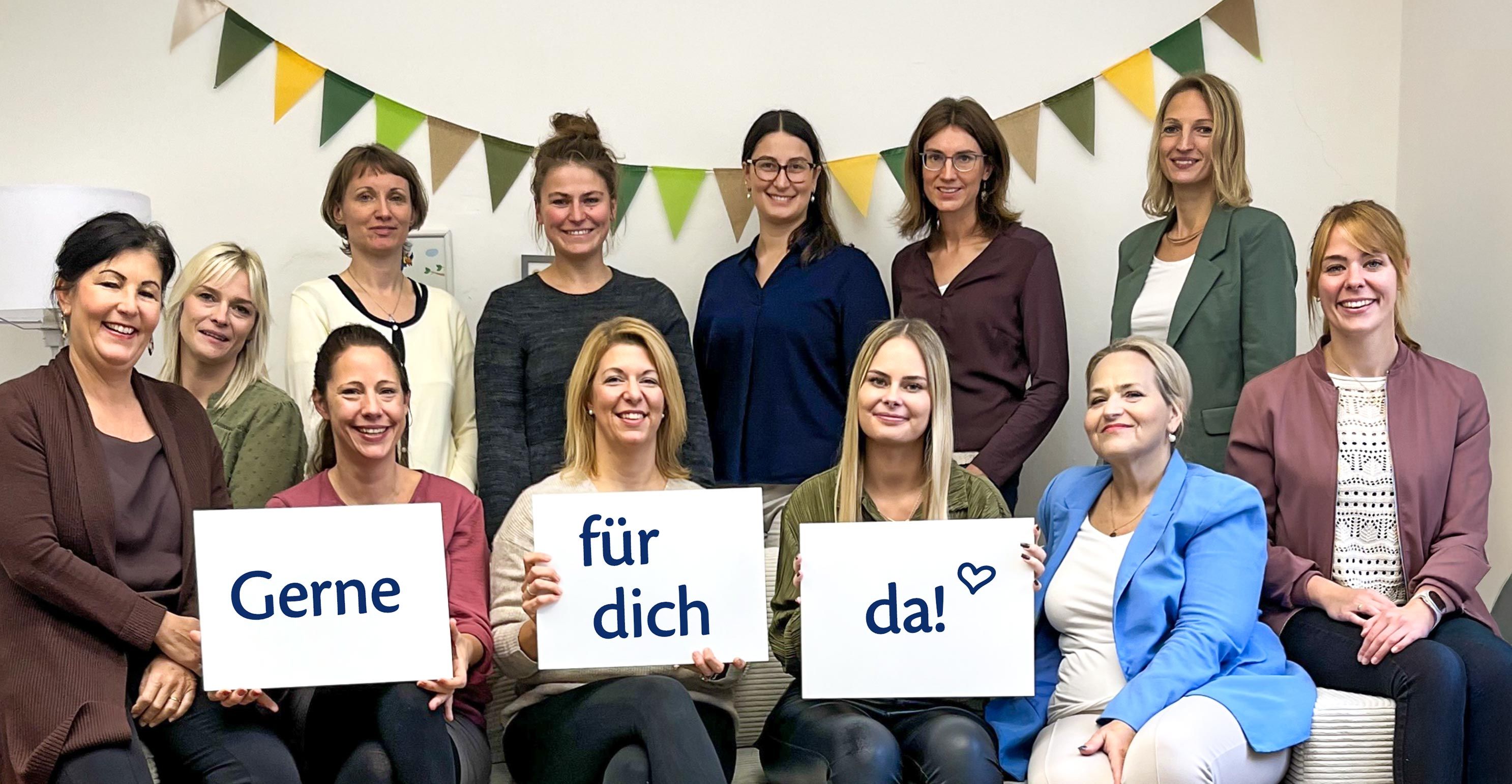 Das Bild zeigt eine Gruppe von zwölf Frauen, die vor einem hellen Hintergrund posieren. Sie halten Schilder mit den Worten "Gerne", "für dich" und "da!" in der Hand.