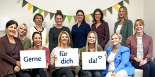 Das Bild zeigt eine Gruppe von zwölf Frauen, die vor einem hellen Hintergrund posieren. Sie halten Schilder mit den Worten "Gerne", "für dich" und "da!" in der Hand.