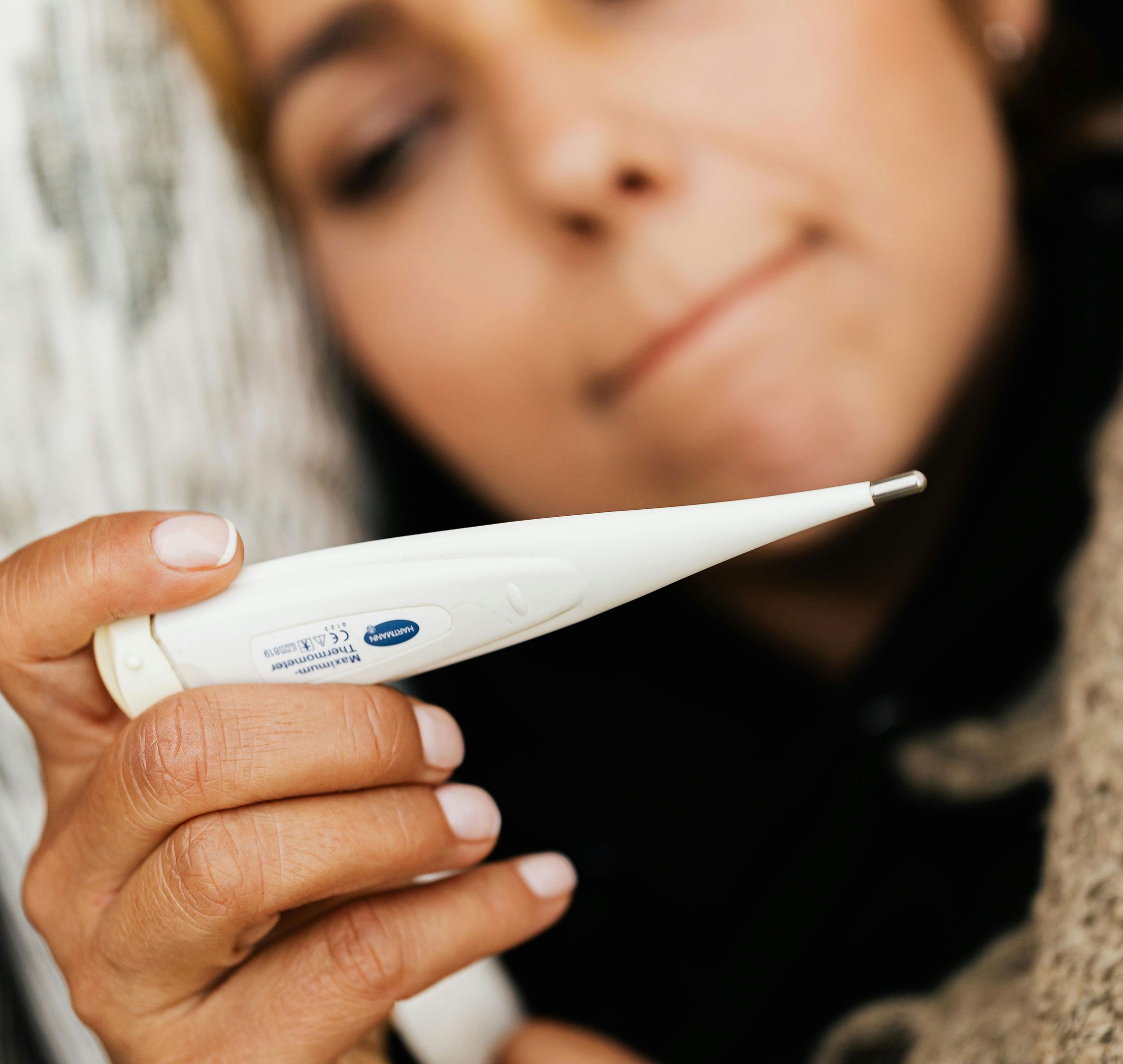 Woman closely checking a digital thermometer, illustrating basal body temperature tracking for family planning.