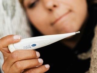 Woman closely checking a digital thermometer, illustrating basal body temperature tracking for family planning.