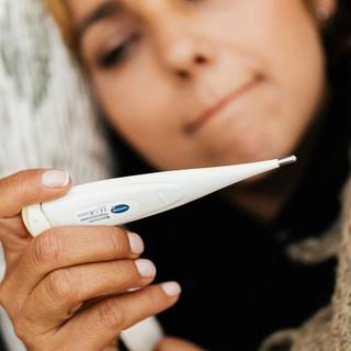 Woman closely checking a digital thermometer, illustrating basal body temperature tracking for family planning.