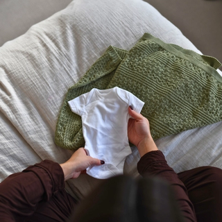 Expecting mum holding out baby onesie on bed