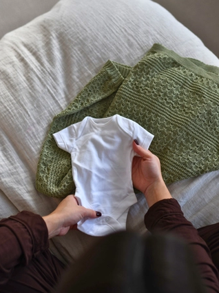 Expecting mum holding out baby onesie on bed