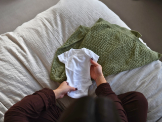 Expecting mum holding out baby onesie on  bed