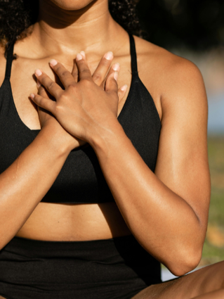Woman sat on exercise mat outside with her hands resting on top of each other over her chest