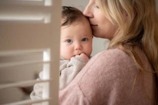 baby held in woman's arms, she seems to be smelling her baby's head and the baby is staring at the camera
