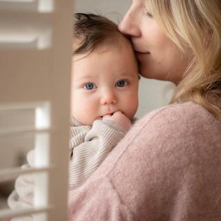 baby held in woman's arms, she seems to be smelling her baby's head and the baby is staring at the camera.