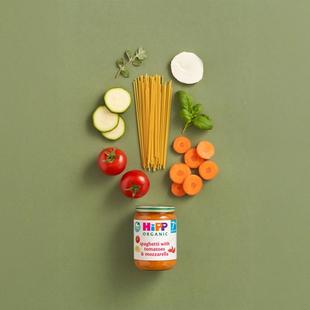 HiPP Organic Spaghetti with Tomatoes & Mozzarella jar surrounded by fresh tomatoes, courgette, carrots, spaghetti and herbs on green