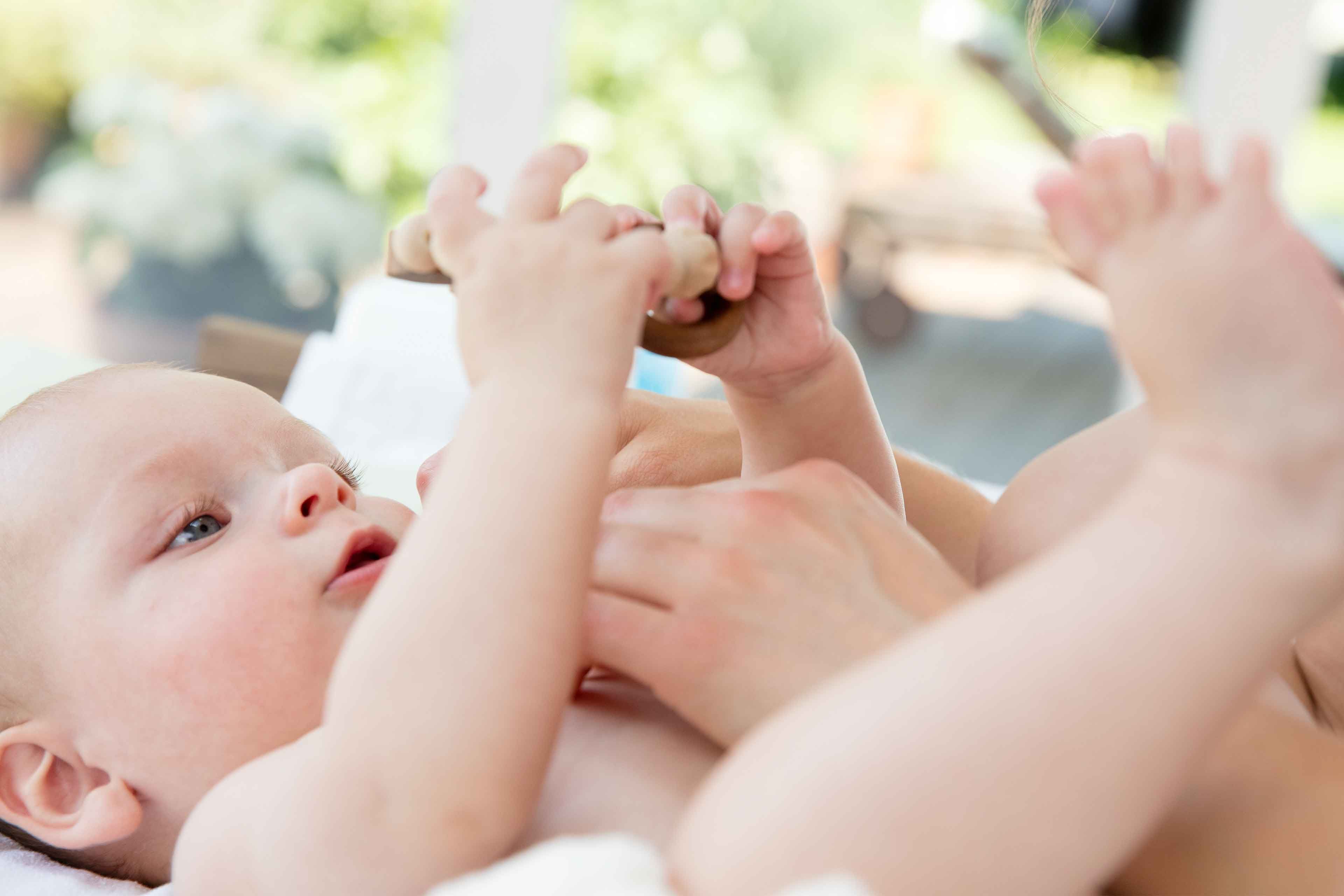Eine Nahaufnahme des Gesichts und der Hände eines Babys, wobei der Schwerpunkt auf den Augen des Babys und der sanften Berührung durch die Hand eines Erwachsenen liegt.